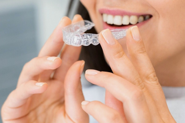 a woman holding her Invisalign tray in front of her mouth.